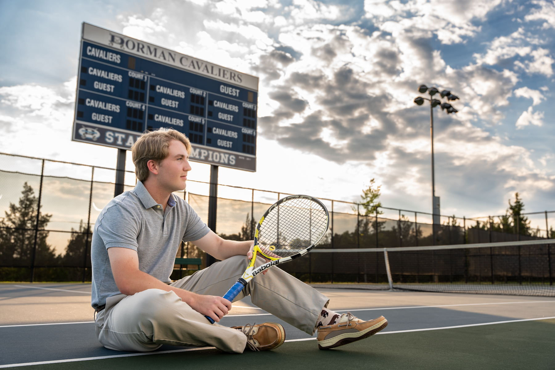 Dorman high school senior sitting for a pose with his tennis racket on the Dorman high school tennis court for high school senior portraits taken by Taylor johnson photography